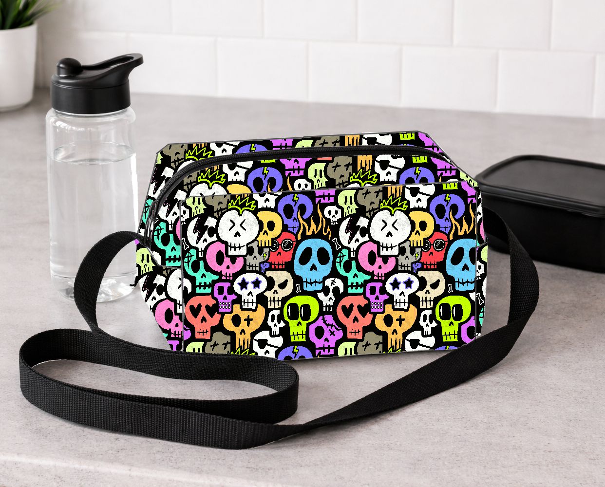 Bolsa tiracolo com padrão colorido de crânios e alça preta sobre bancada cinza