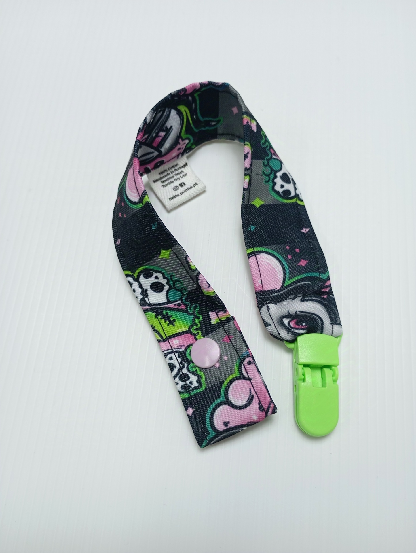 Prendedor de chupeta com padrão colorido e clip verde.