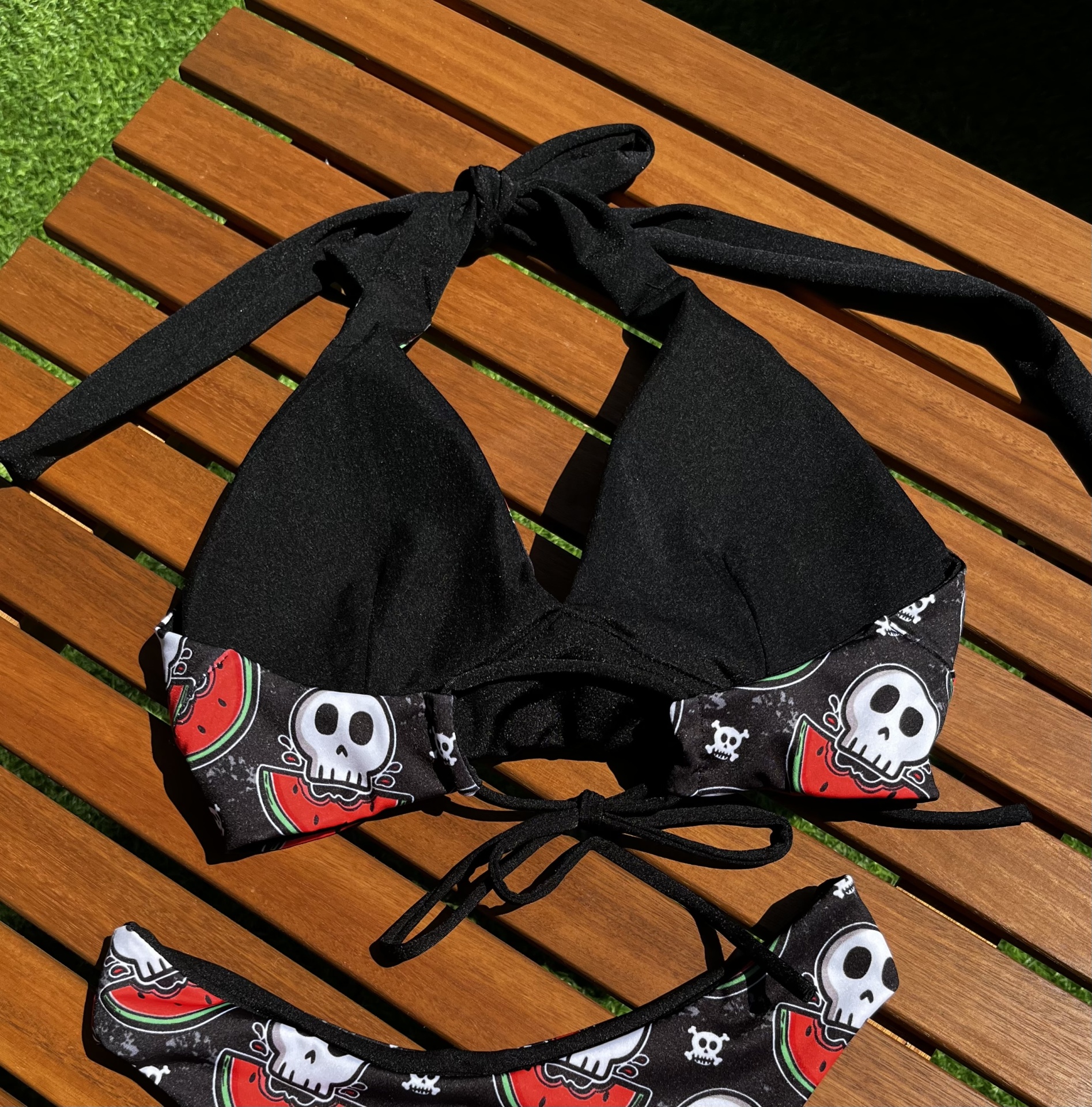 Biquíni preto com padrão de caveiras e melancias sobre madeira