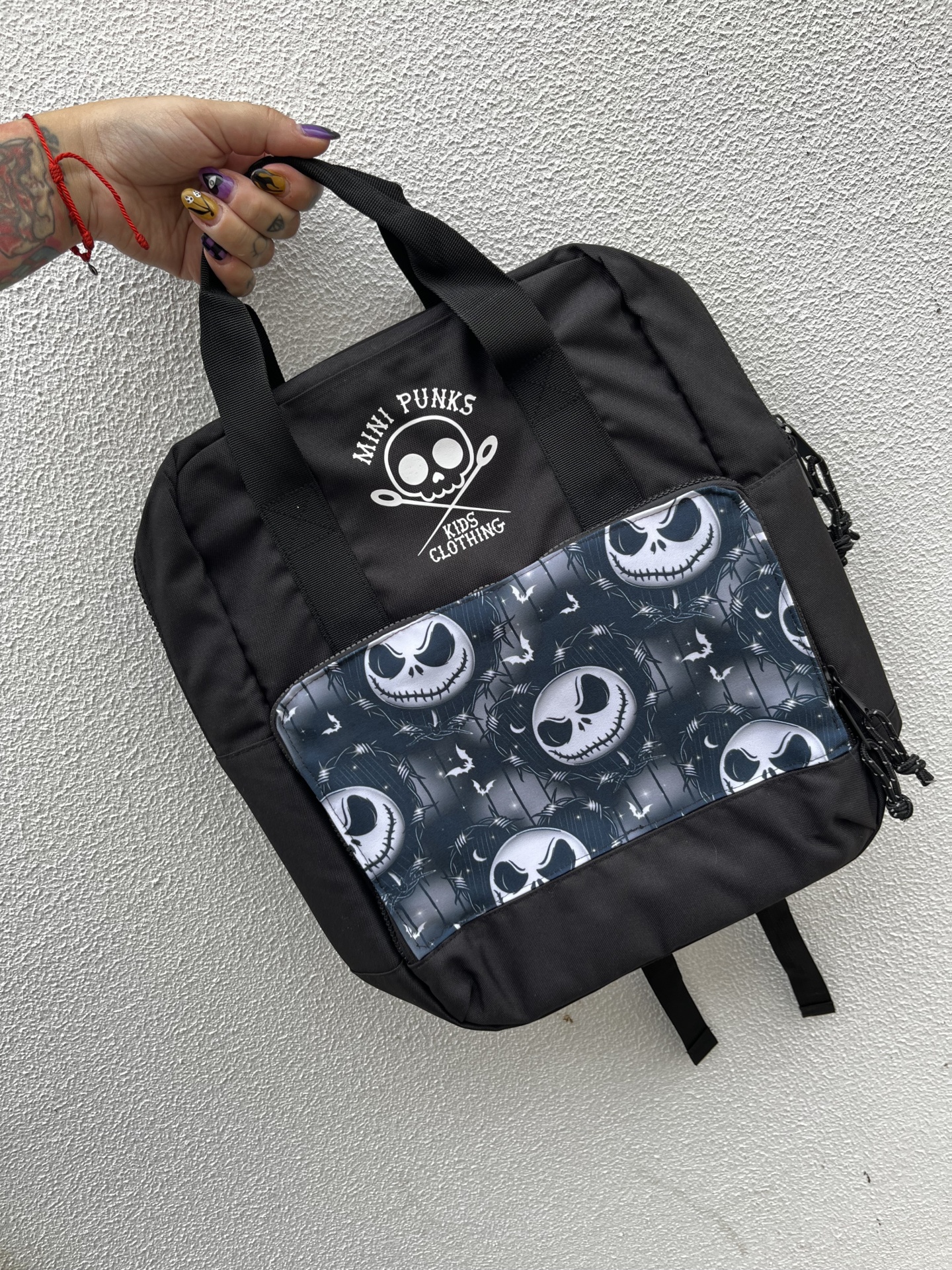 Mochila preta infantil com bolso com padrão de caveiras e texto MINI PUNKS KIDS CLOTHING