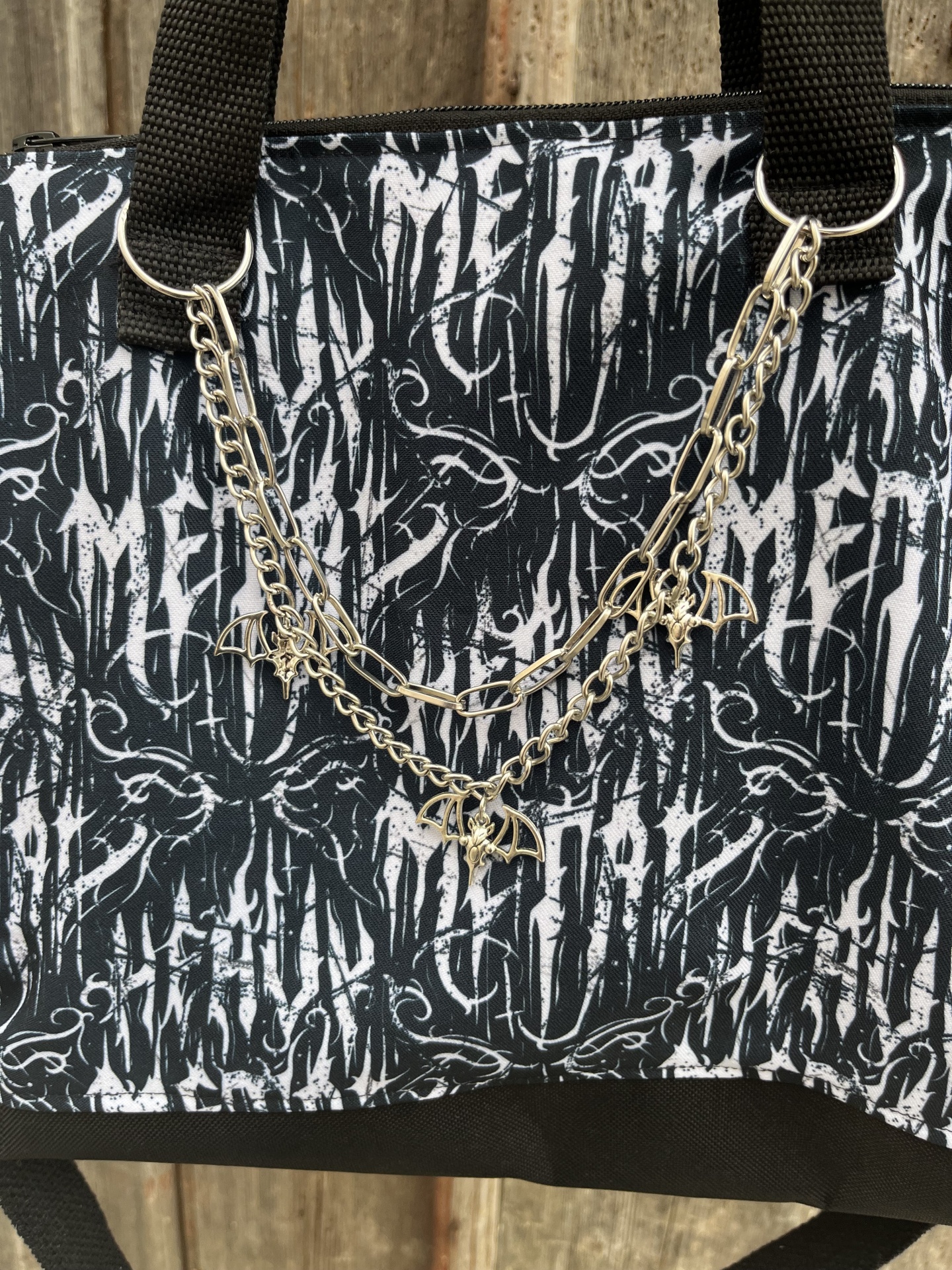 Saco preto e branco com padrão gráfico e correntes douradas com morcegos.