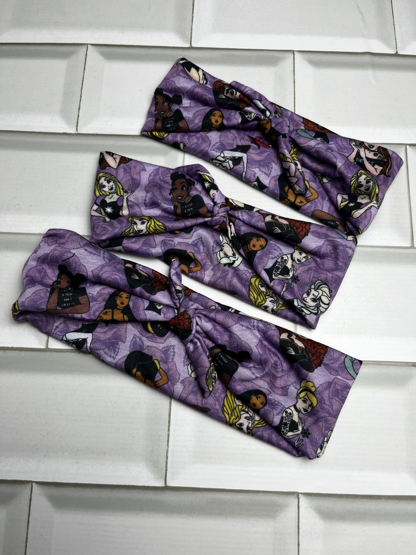 Três faixas elásticas roxas com padrão de rostos femininos coloridos sobre azulejos brancos