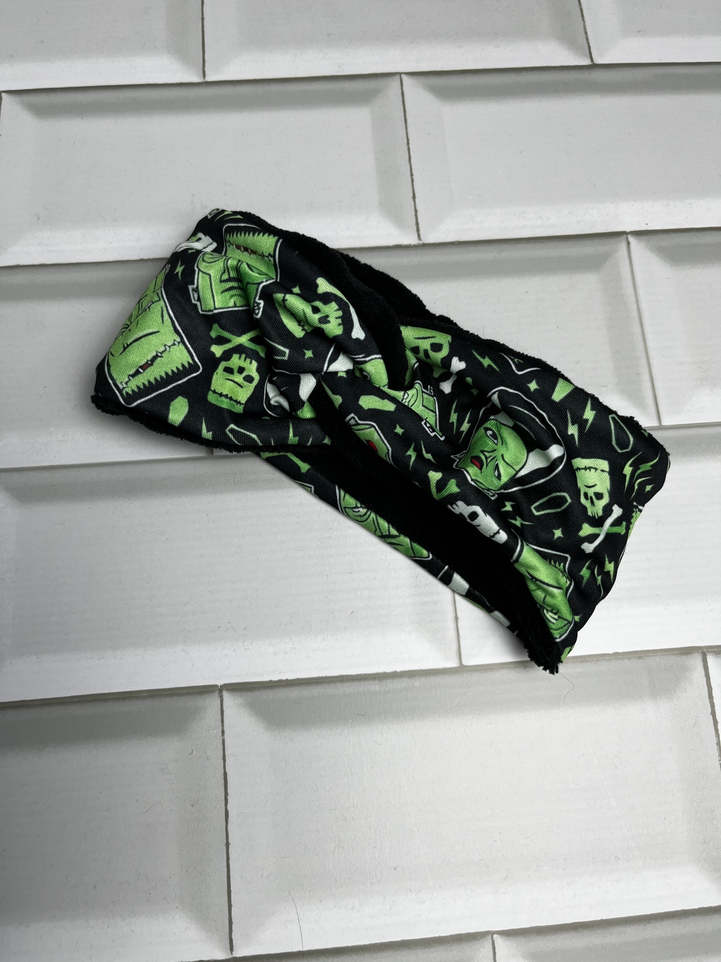 Faixa de cabeça preta com padrão verde de Frankenstein e caveiras colocada sobre azulejos brancos