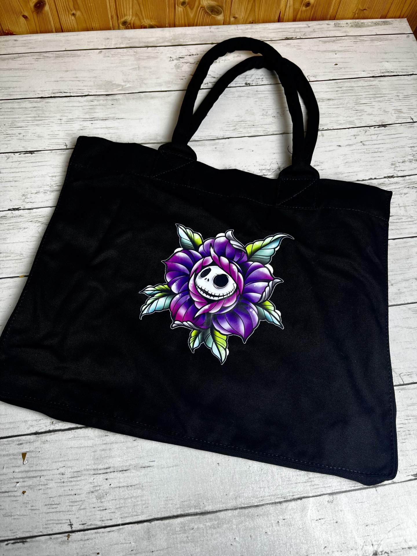 Saco preto de tecido com estampa de flor roxa e caveira no centro