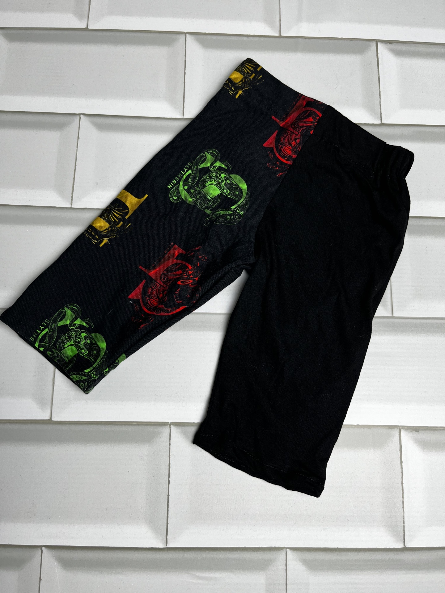 Calções pretos com padrão colorido numa perna sobre azulejos brancos