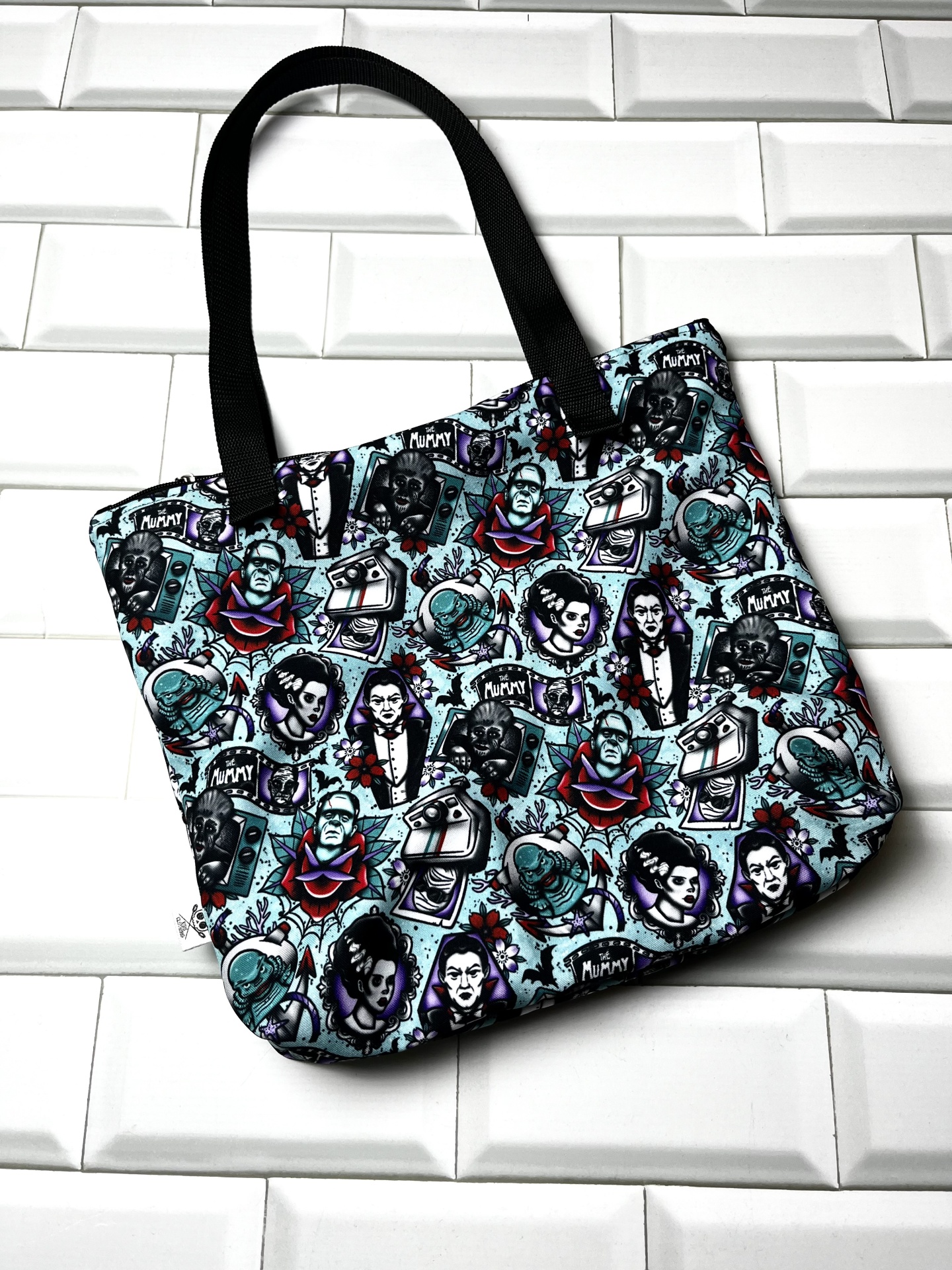 Mala tote com padrão de monstros clássicos de filmes de terror, fundo branco e alças pretas