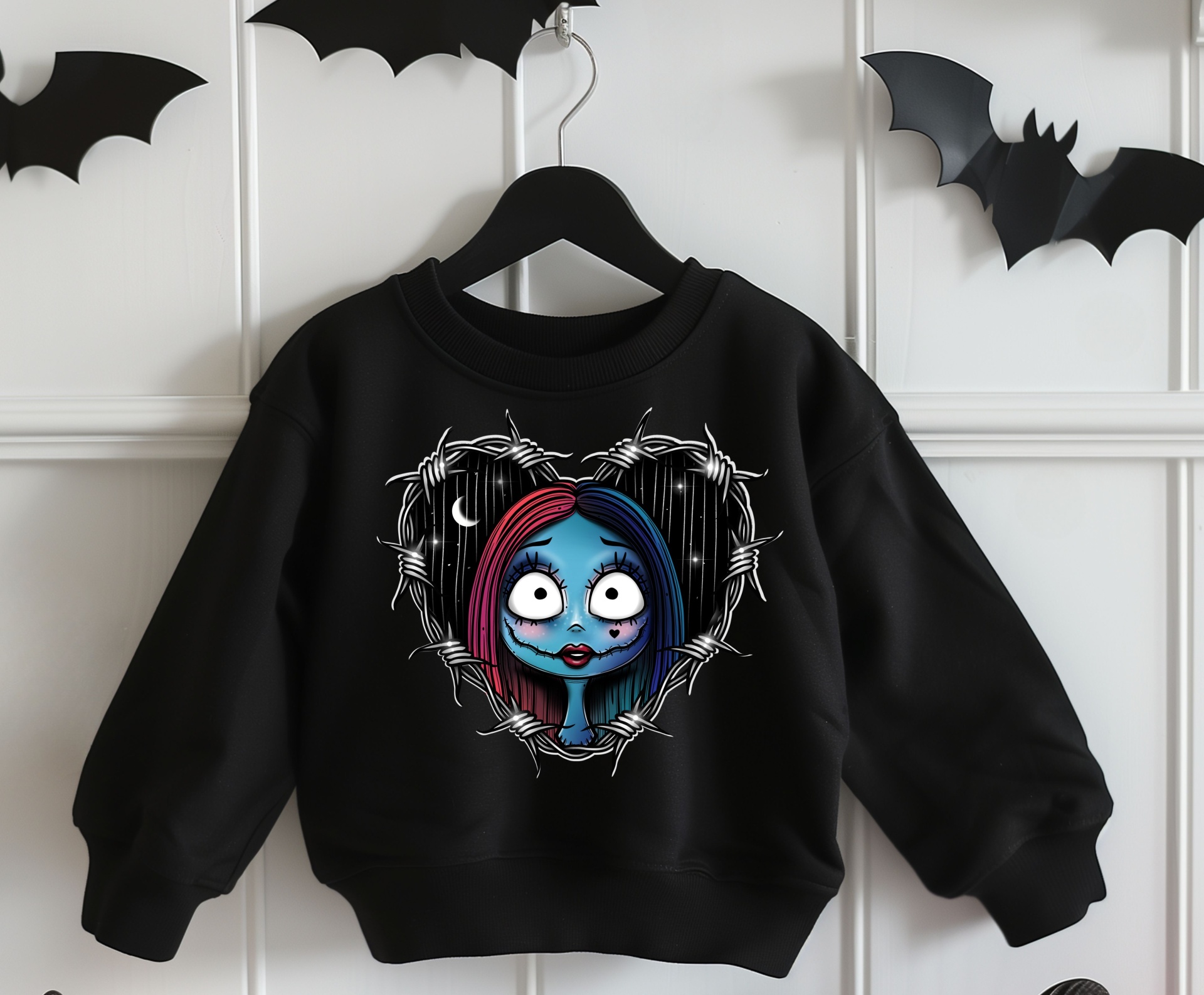Sweatshirt preta infantil com estampa de personagem azul e vermelho e arame farpado, pendurada com morcegos de papel ao fundo
