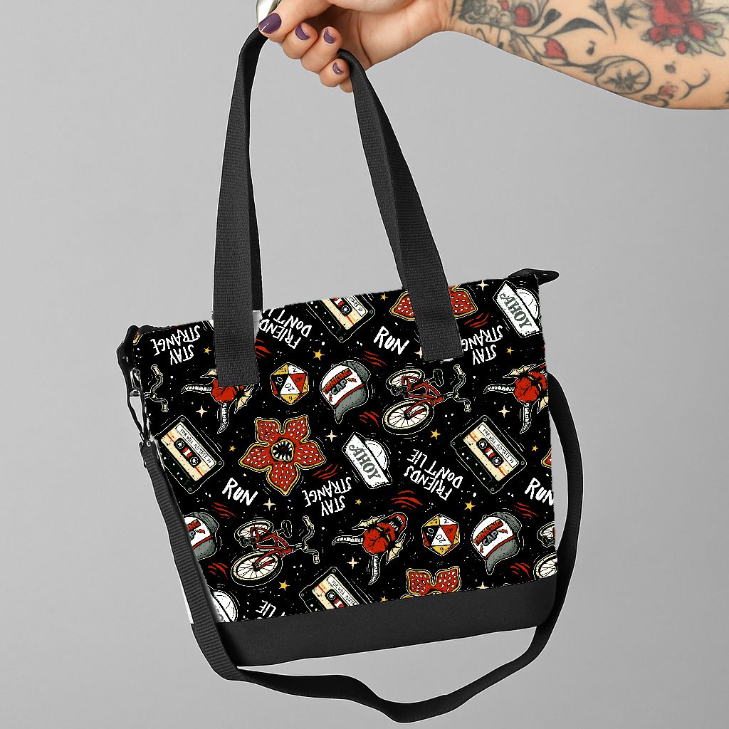 Mala preta com padrão colorido e frases em inglês com mão tatuada a segurar