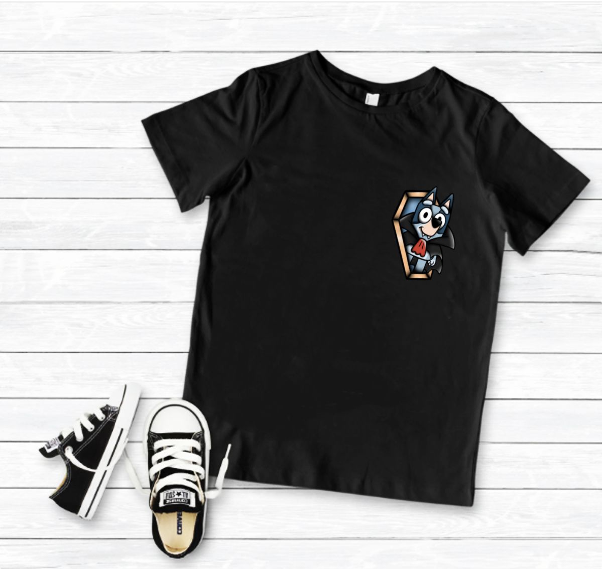 T-shirt preta com estampa de personagem animado e sapatilhas pretas com branco sobre madeira branca