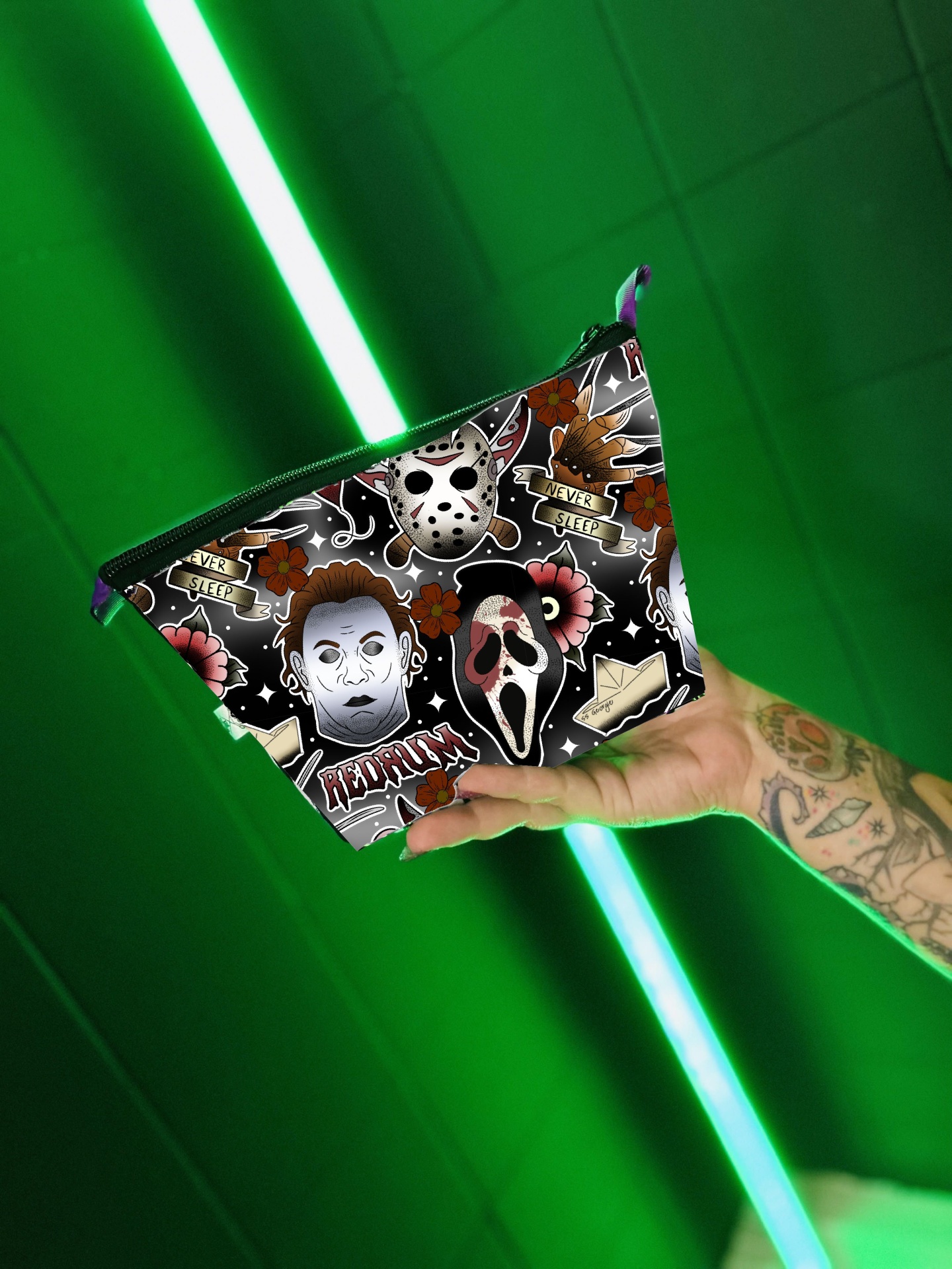 Bolsa de maquilhagem com padrão de personagens de filmes de terror segurada por uma mão tatuada