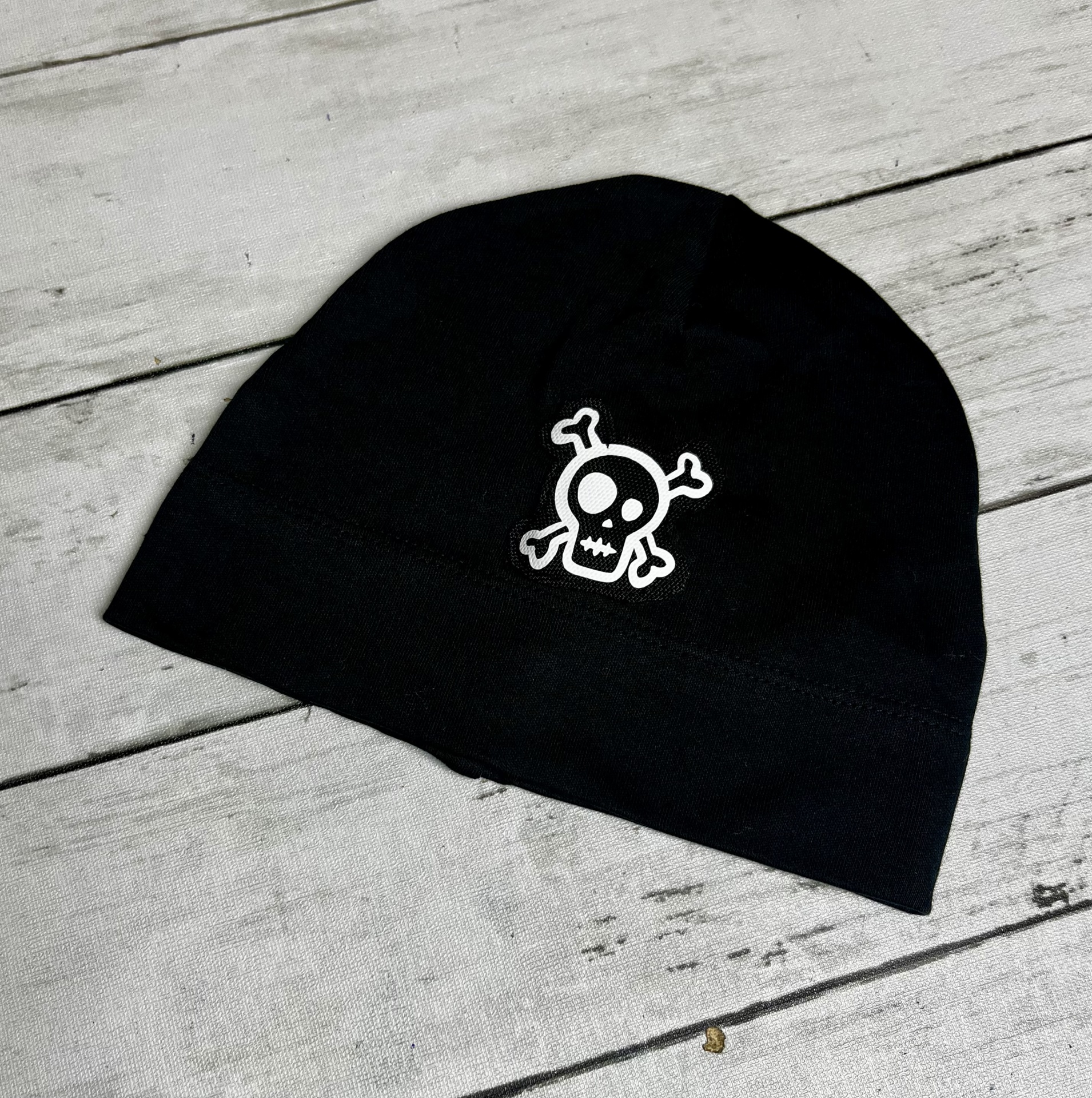Gorro preto com estampa de caveira branca sobre fundo de madeira clara.