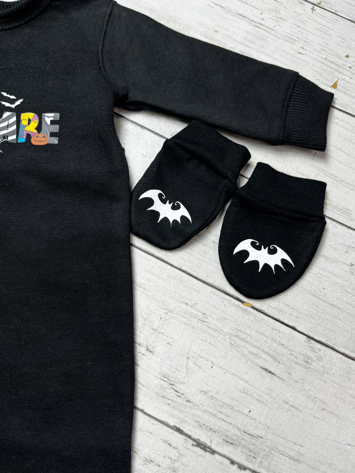 Conjunto preto para bebé com estampa colorida e luvas com símbolo de morcego.