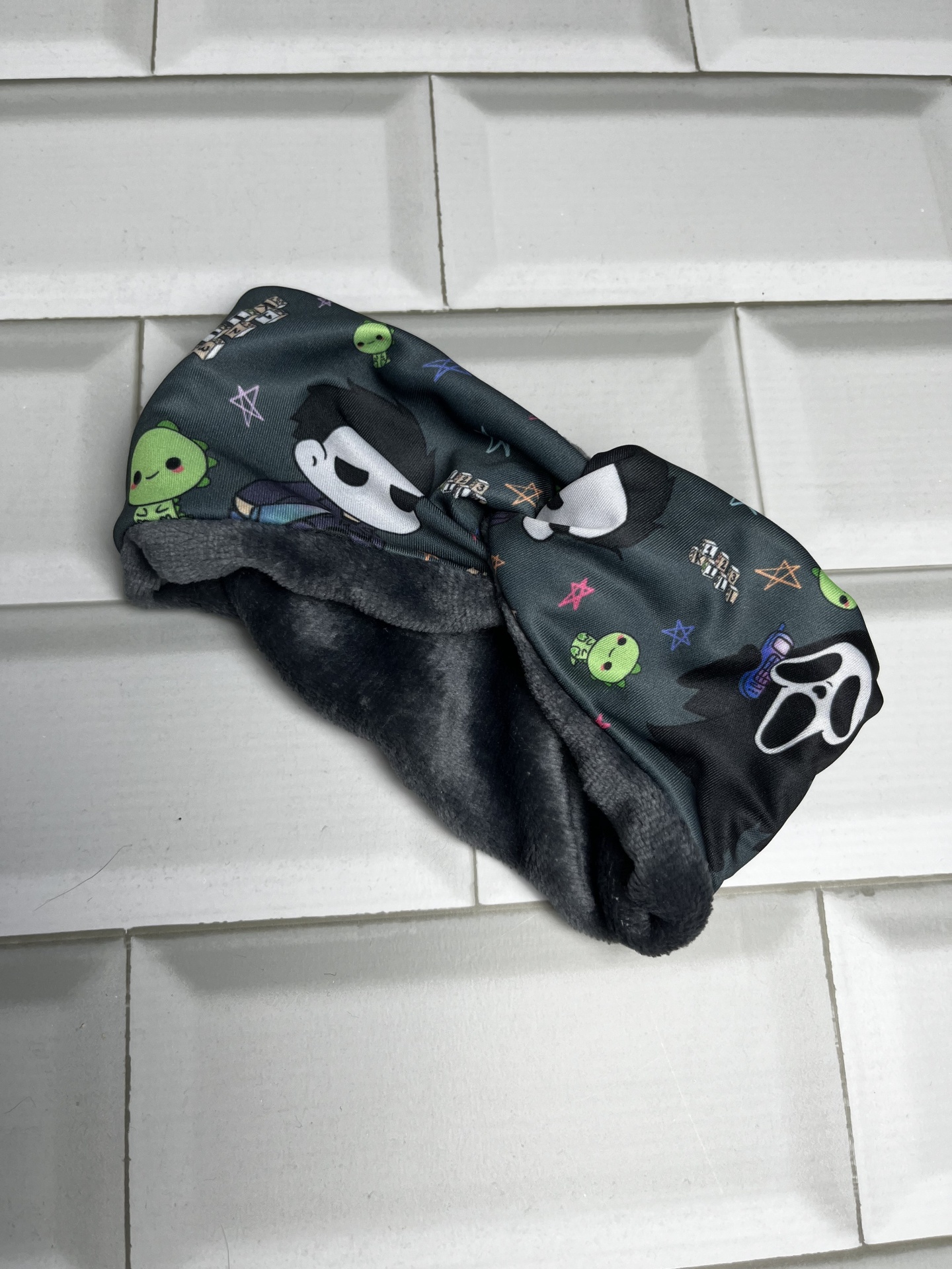 Faixa preta com estampado de máscaras e aliens verdes sobre azulejos brancos