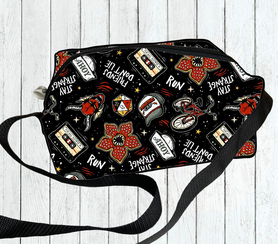 Mala preta com padrão colorido de flores, bicicletas, dados, fitas cassete, bonés e textos sobre fundo de madeira clara