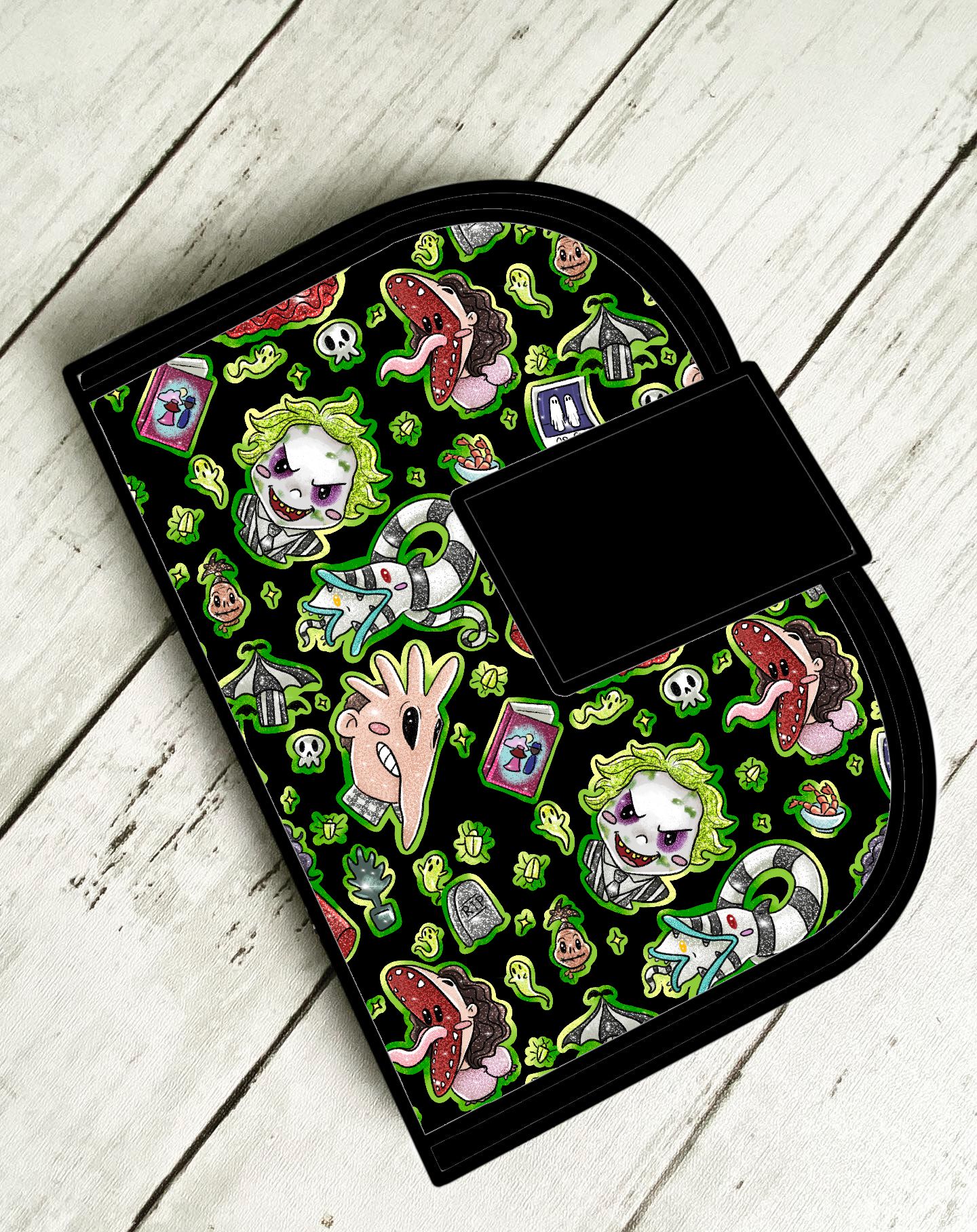 Carteira preta com estampado cartoon colorido sobre superfície de madeira branca