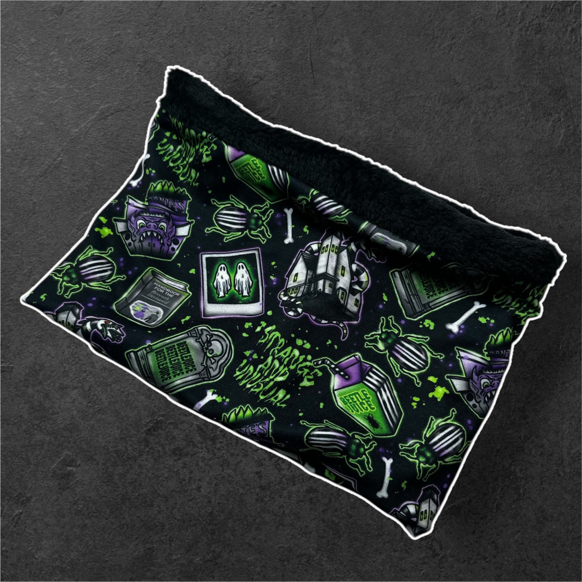 Cachecol tubular preto com padrão verde, roxo e branco, incluindo fantasmas, besouros e texto 'BEETLE JUICE'.