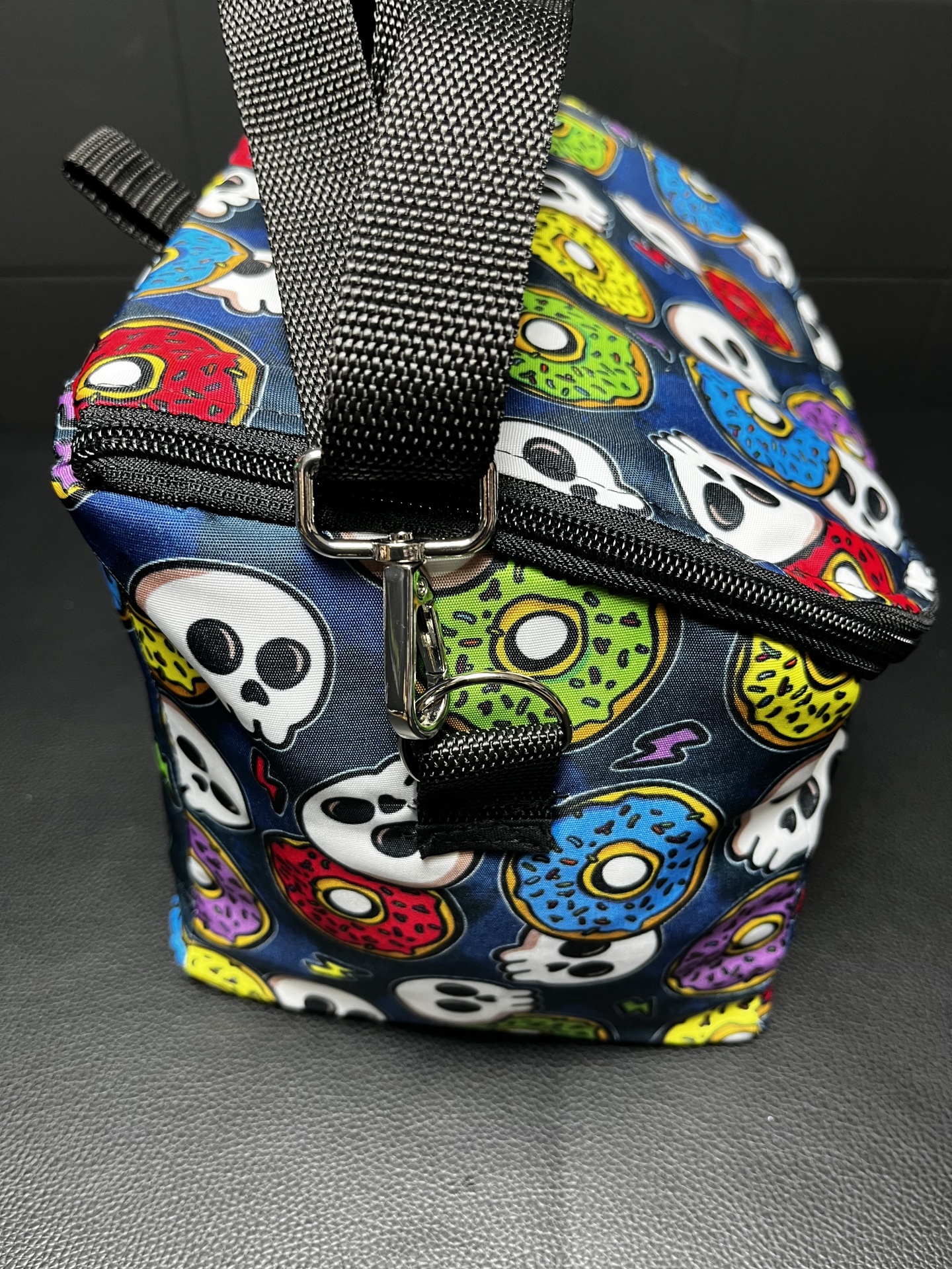 Bolsa de mão com padrão de donuts e caveiras coloridos sobre fundo azul escuro