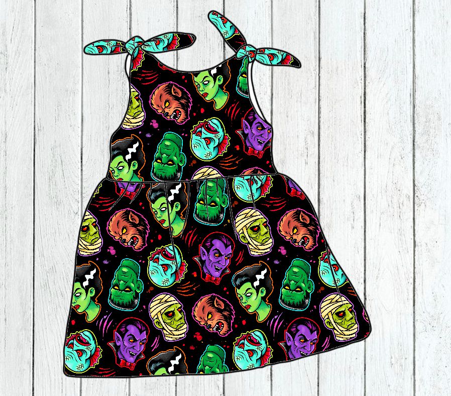 Vestido infantil preto com padrão colorido de cabeças de monstros e alças de amarrar nos ombros