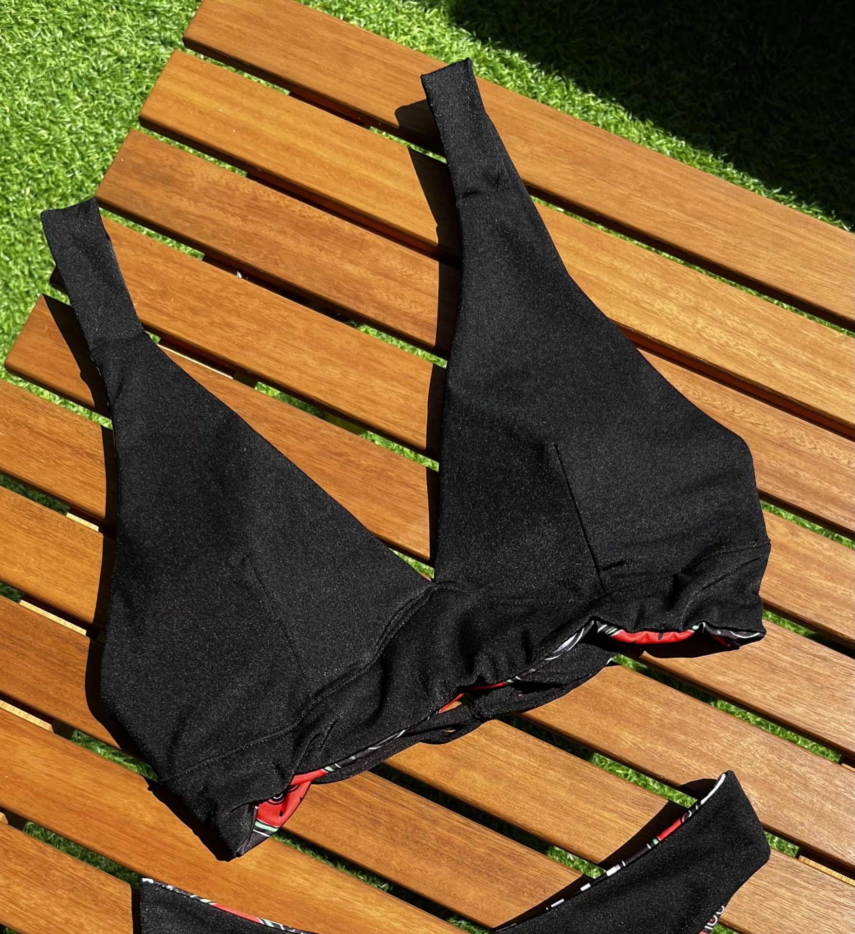 Parte superior de fato de banho preto sobre madeira e relva