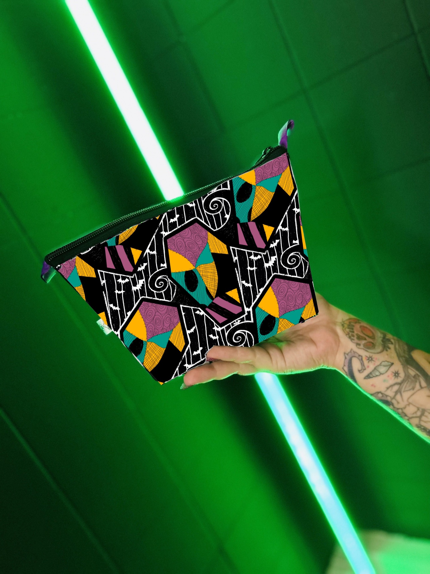 Bolsa pequena colorida com padrão geométrico segurada por mão tatuada em fundo verde
