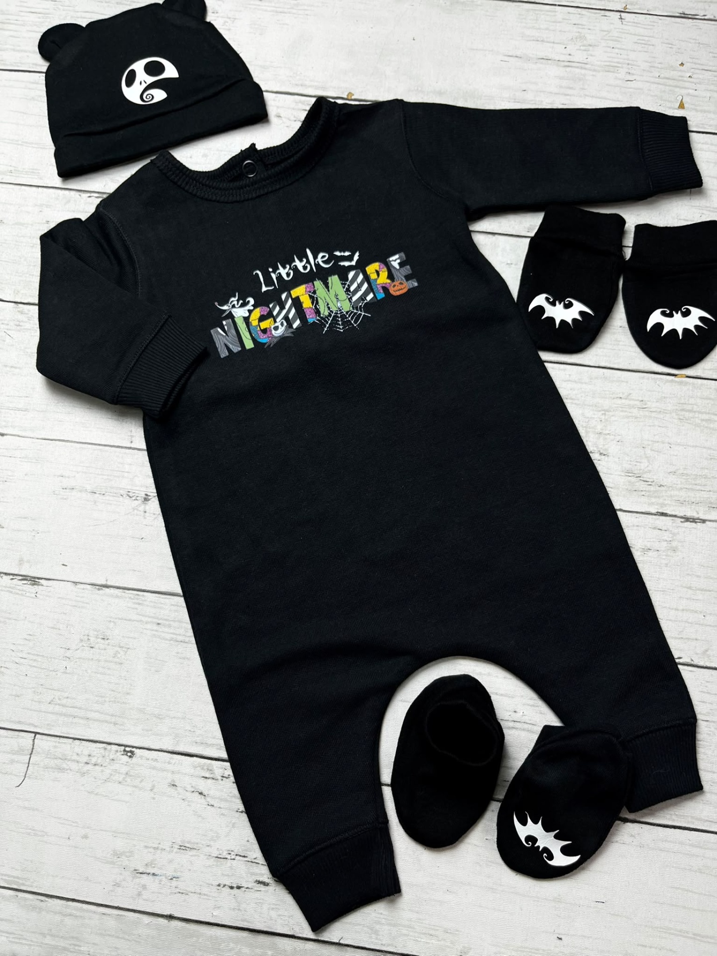 Conjunto de bebé preto com padrão Little NIGHTMARE e acessórios temáticos em fundo de madeira branca
