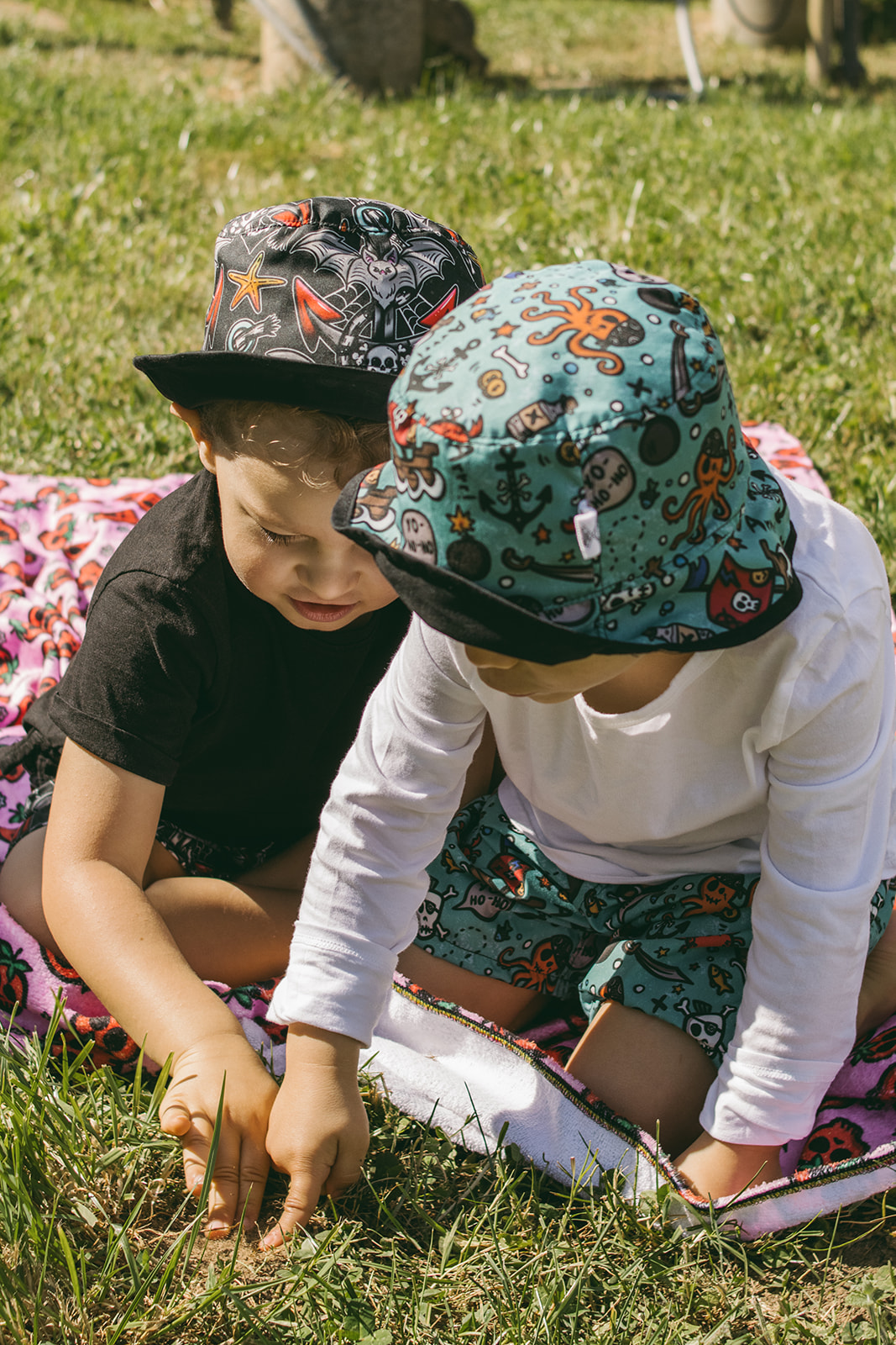 Dois meninos sentados na relva com chapéus estampados coloridos e roupas casuais