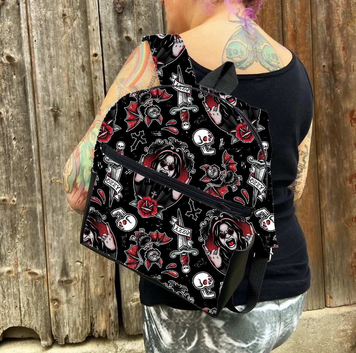 Mochila preta com padrão de caveiras e rosas usada por pessoa com regata preta e tatuagens