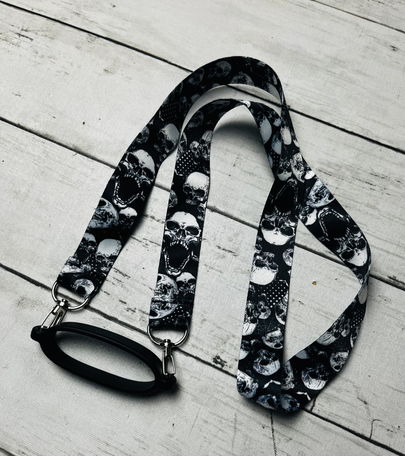 Cordão para óculos preto com padrão de caveiras e suporte metálico
