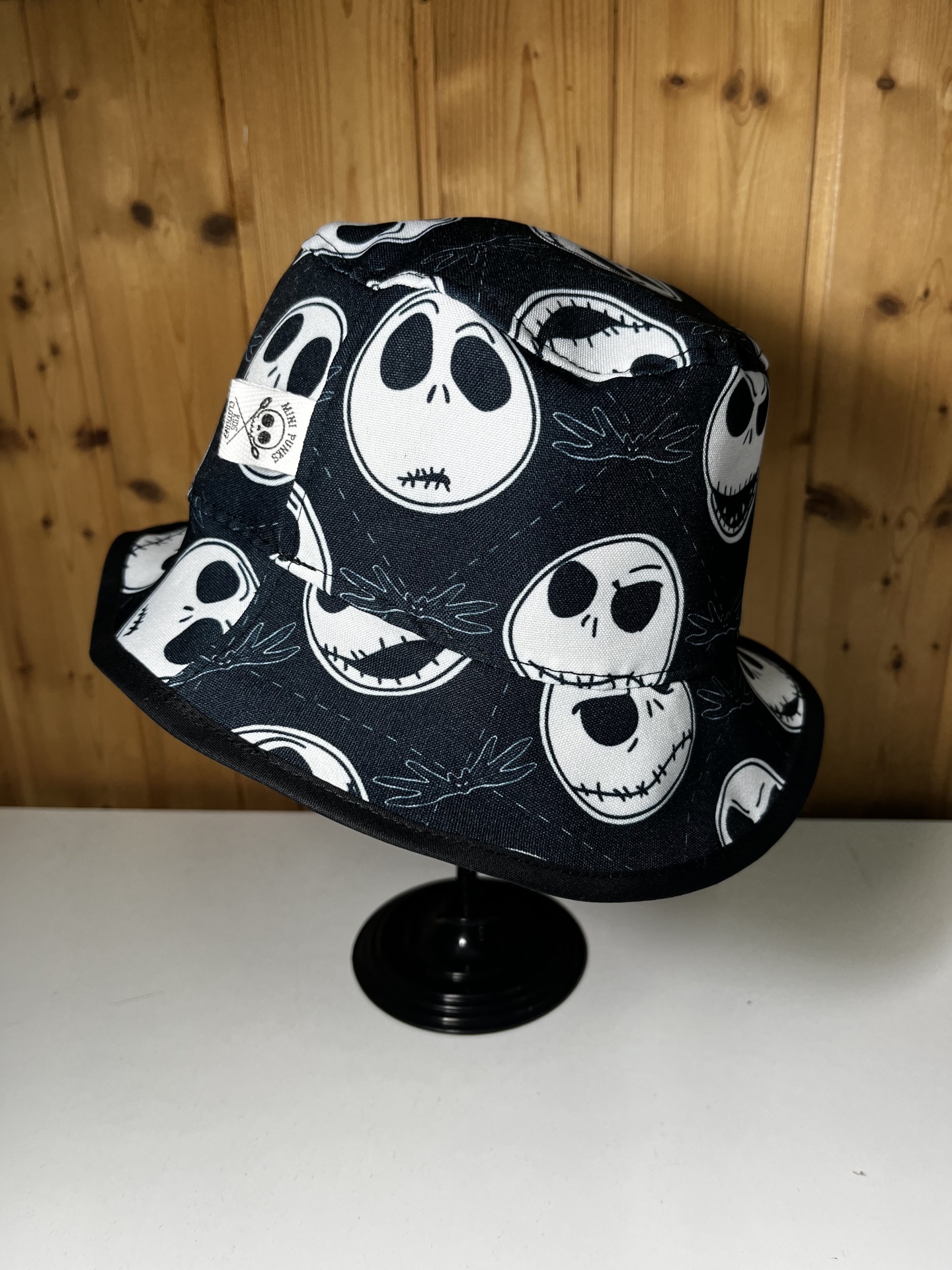 Chapéu bucket preto com padrão de caveiras brancas em fundo de madeira