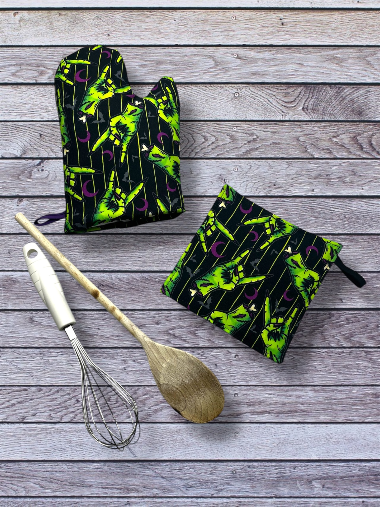 Utensílios de cozinha em tecido estampado com luva térmica, pega para forno, colher de pau e batedor sobre madeira.