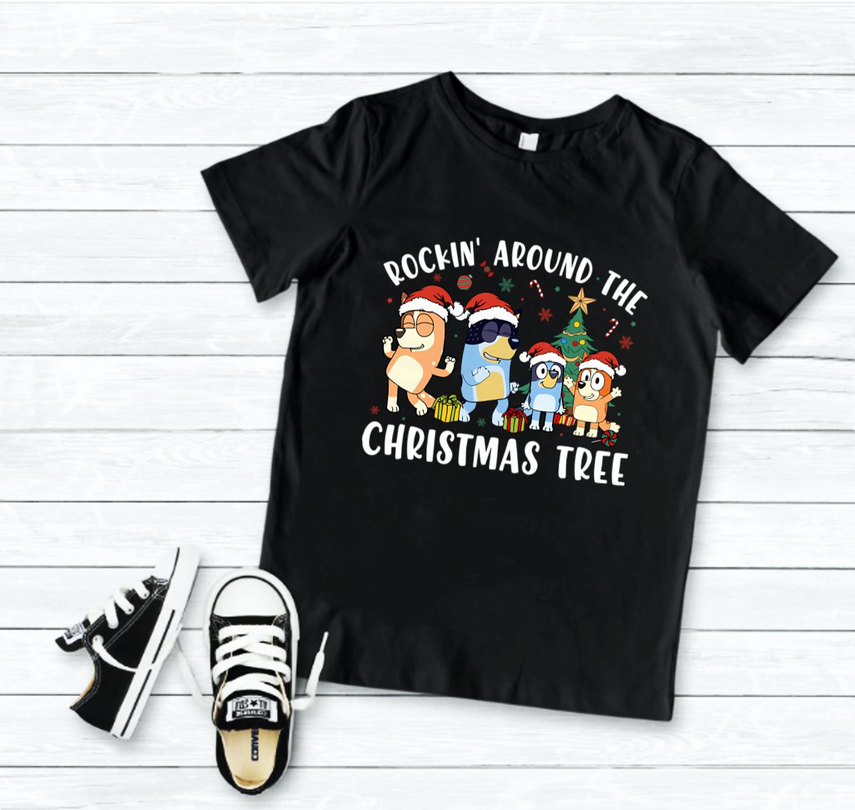 T-shirt preta com estampa de Natal e ténis pretos e brancos sobre chão de tábuas de madeira
