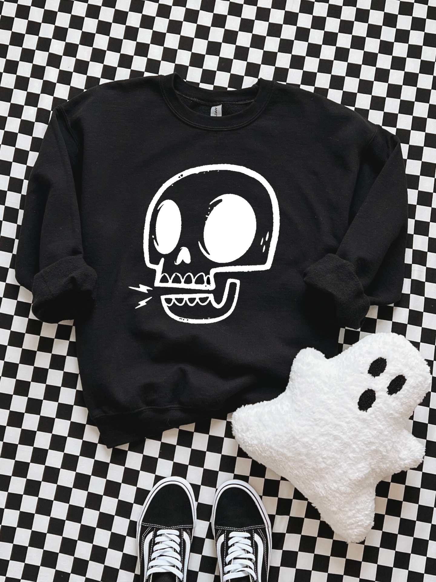 Sweatshirt preta com estampa de crânio branco sobre padrão xadrez com almofada de fantasma e sapatilhas