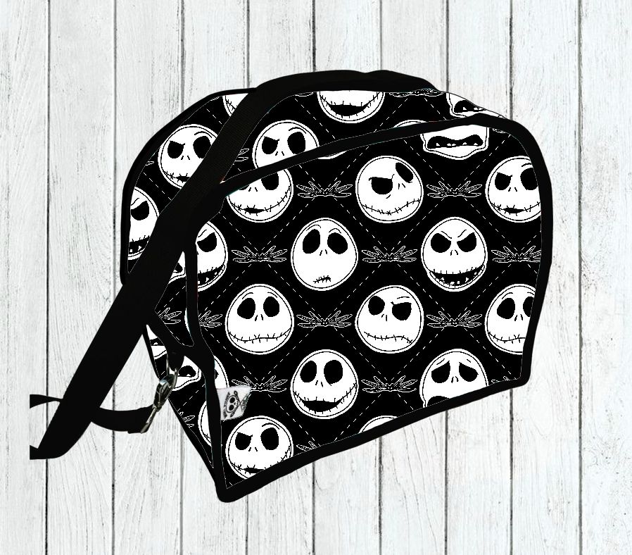 Mala preta com padrão de rostos brancos sobre fundo de madeira clara