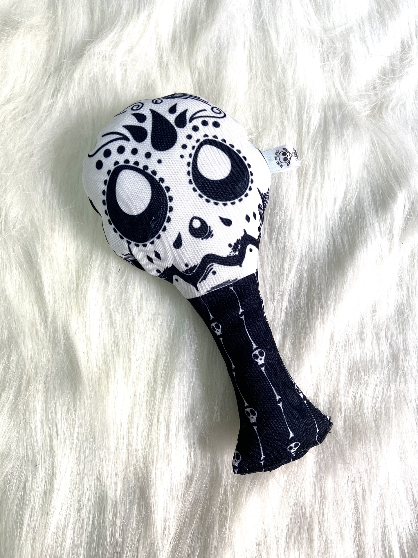 Brinquedo de tecido preto e branco com estampa de caveira decorativa colocado sobre superfície branca fofa