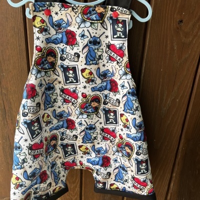 Macacão infantil com padrão de Stitch pendurado num cabide azul contra porta de madeira