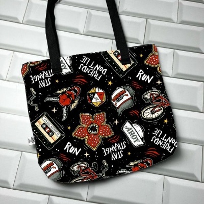 Mala de tecido preta com desenhos e frases coloridas e alças pretas sobre chão de azulejos brancos