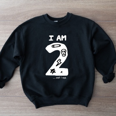 Camisola preta com texto e desenhos brancos sobre superfícies de madeira clara.