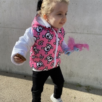 Criança com casaco rosa e branco, calças pretas e sapatilhas brancas segurando brinquedo colorido