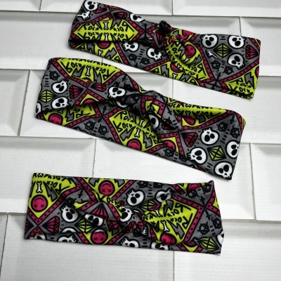 Três faixas de cabelo coloridas com estampado de caveiras e triângulos sobre azulejos brancos