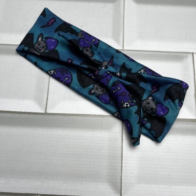 Faixa de cabelo azul escuro com padrão de morcegos e caveiras sobre azulejos brancos