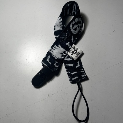 Prendedor de chupeta preto e branco com caveiras e teias de aranha