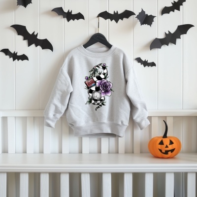 Camisola cinza clara com estampa de bola de futebol, flor roxa e garrafa, pendurada em cabide, com morcegos de papel e abóbora de Halloween.