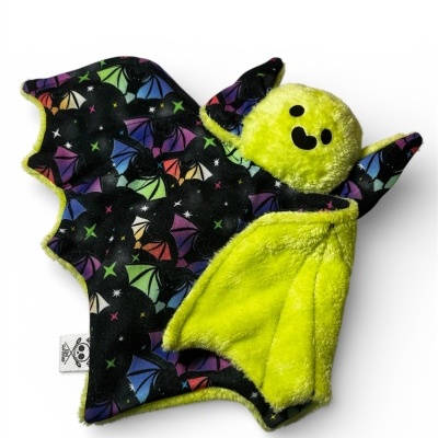 Brinquedo de morcego de pelúcia amarelo com asas pretas coloridas e padrão de morcegos.