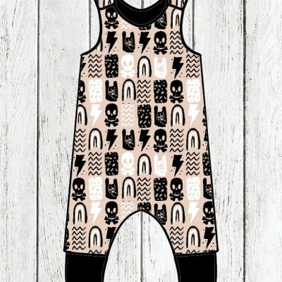 Macacão infantil com padrão de caveiras, raios e arcos em bege, preto e branco sobre fundo de madeira branca