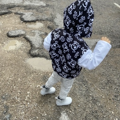 Criança com casaco preto e branco com capuz e calças cinza em pavimento