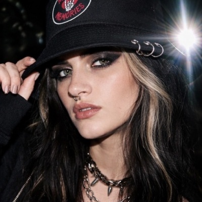 Mulher com boné preto decorado com piercings metálicos e bordado vermelho e branco