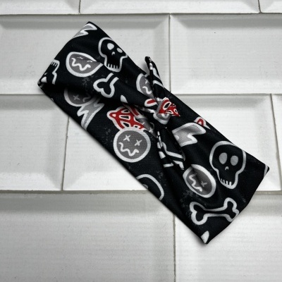 Faixa de cabelo preta com padrão de caveiras e ossos sobre azulejos brancos