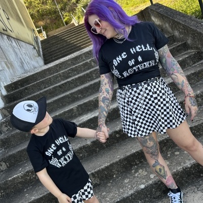 Duas pessoas com t-shirts pretas com texto branco, caleções xadrez preto e branco, calçam ténis e estão numa escadaria ao ar livre.