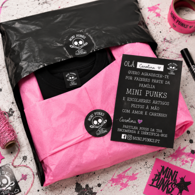 Pacote com roupa infantil embrulhada em papel rosa e etiqueta MINI PUNKS com cartão de agradecimento em português
