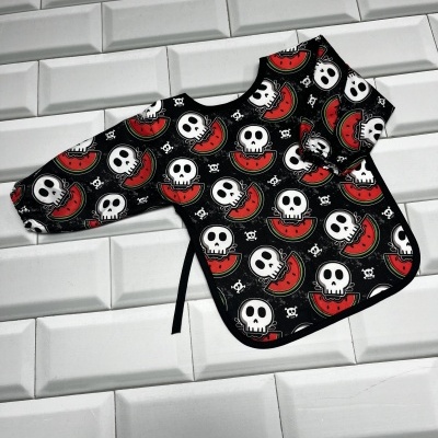 Babete de mangas compridas com padrão de caveiras e melancias sobre azulejos brancos